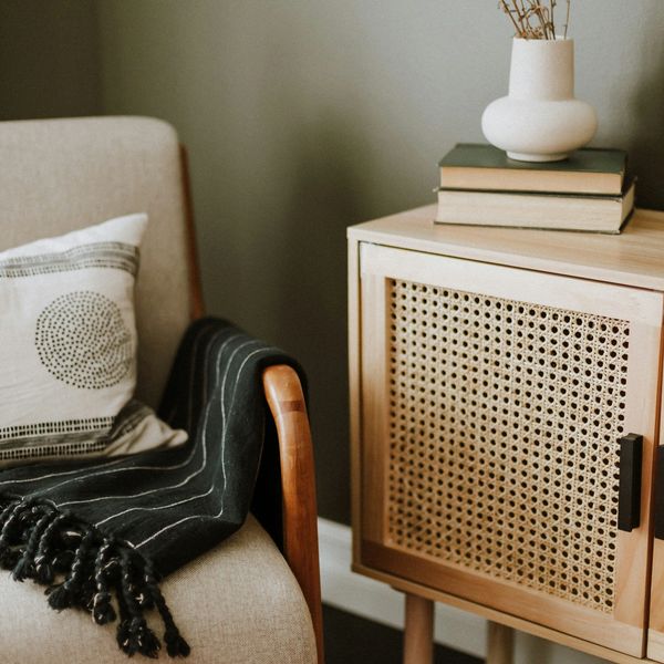 Cozy chair in Grover Beach with pillow and blanket next to wooden cabinet with books and vase.