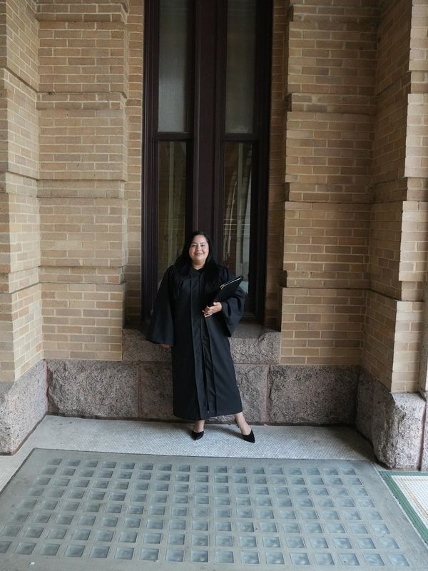 Graduate standing in front of a brick wall.