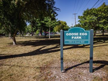 Sign for Goose Egg Park with trees and playground in the background.