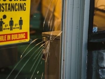 Cracked glass window beside a social distancing sign inside a building.