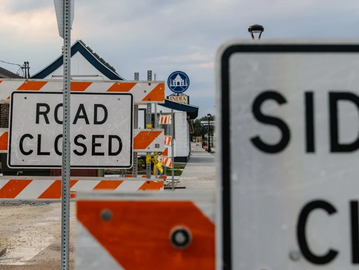 Multiple road and sidewalk closed signs block a street under cloudy skies.