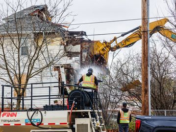 Construction workers demolishing a house with an excavator.