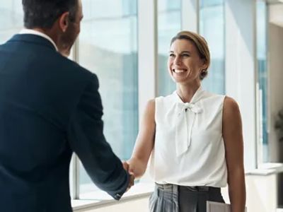 A woman and man shaking hands in a professional setting.