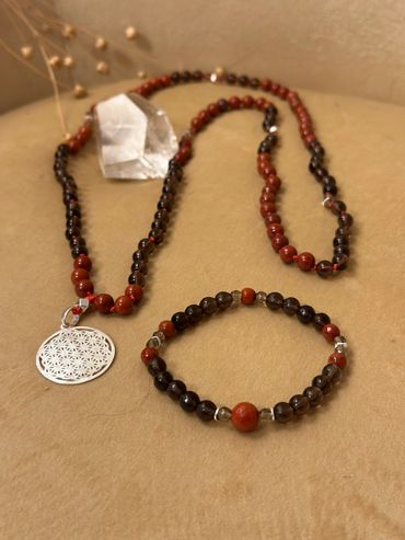 A beaded necklace and bracelet set with red and dark beads on a beige surface.