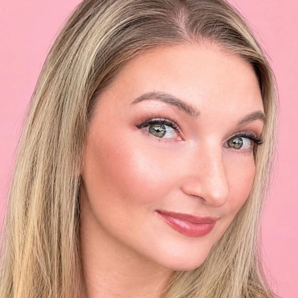 Close-up of a smiling woman with blonde hair against a pink background.
