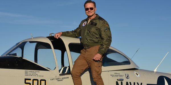 Man in aviator jacket standing by Navy aircraft.