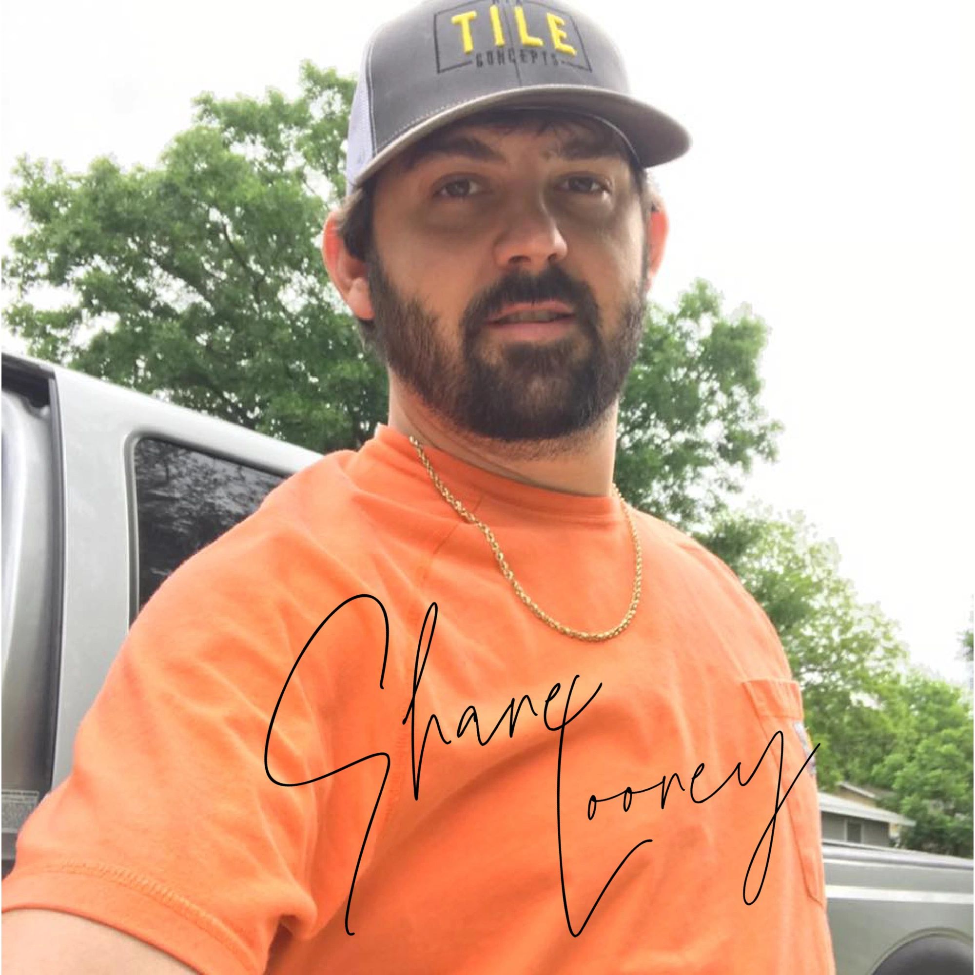 Man with beard wearing a TILE Concepts cap and orange shirt outdoors.