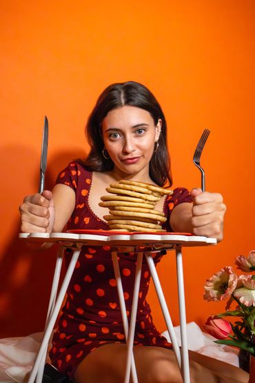 Woman in a red polka dot dress with a knife and fork ready to eat pancakes.