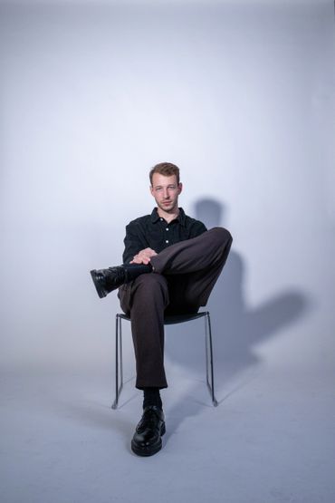 Man sitting confidently on a chair against a plain background.