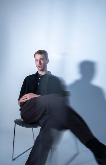 Man in black sitting on a chair with a shadow on the wall.
