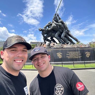 Two men smiling in front of a military statue.