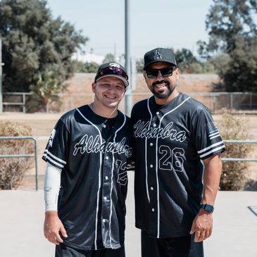 Two men in baseball jerseys smiling outdoors.