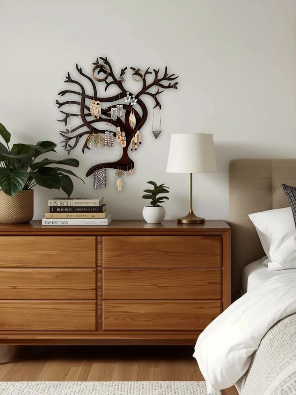 Wooden dresser with plants, lamp, and jewelry tree next to a bed in a cozy bedroom.