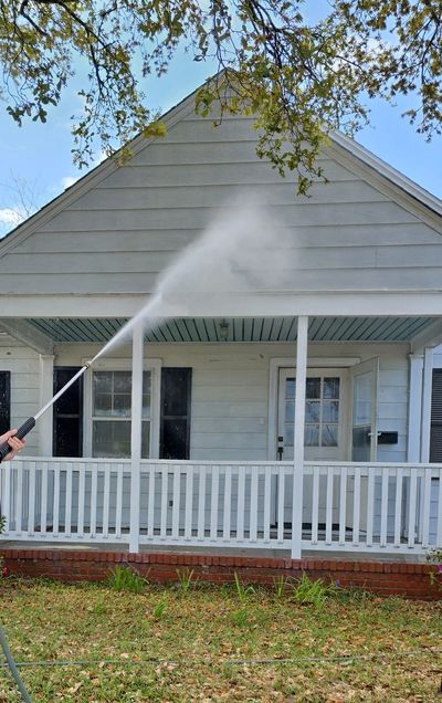 Person pressure washing the porch of a white house.
