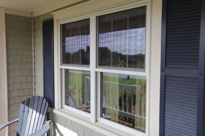 A window with blue shutters on a porch with a chair.