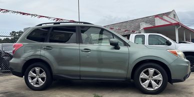 Side view of a green SUV parked outdoors near a white truck.