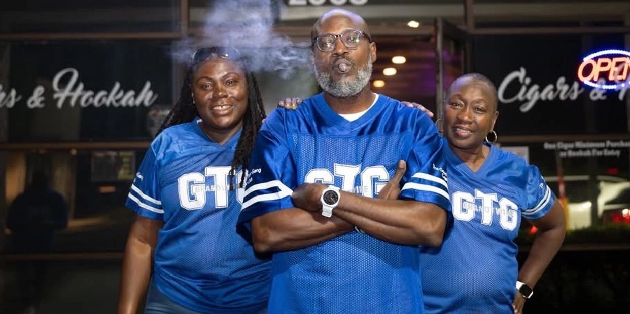 Three people in matching blue GTG shirts posing in front of a cigars and hookah shop.