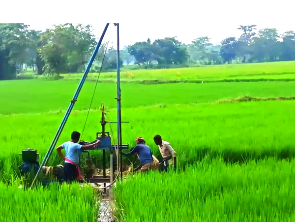 Three men operating a water pump in a lush green paddy field.
