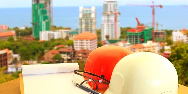 Construction helmets, notepad, and pen on a table with cityscape in background.