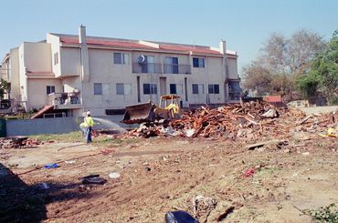 Demolition debris in front of a residential building with a worker and bulldozer.