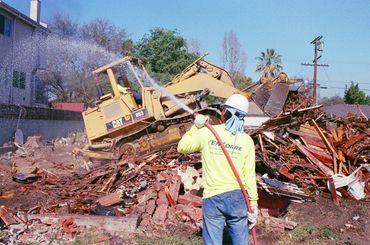 Construction worker overseeing bulldozer clearing debris from demolished building.