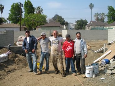 Five construction workers posing at a residential worksite on a sunny day.