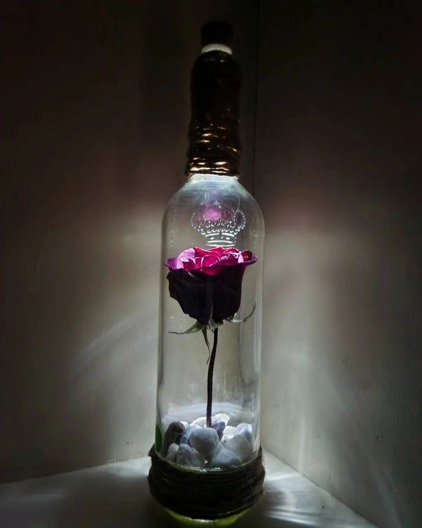 A glowing rose inside a decorative glass bottle with rocks.
