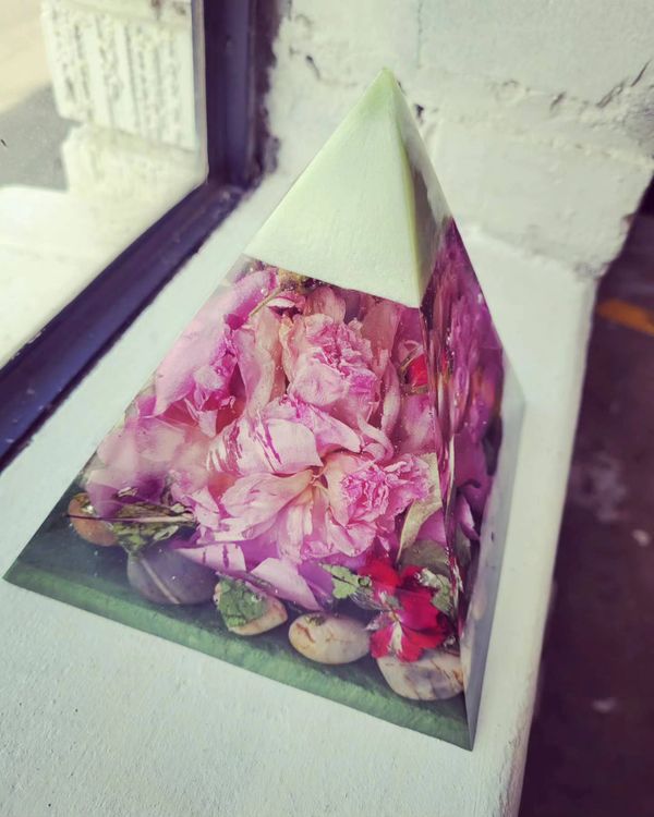 A pyramid-shaped resin piece with pink flowers and stones inside.