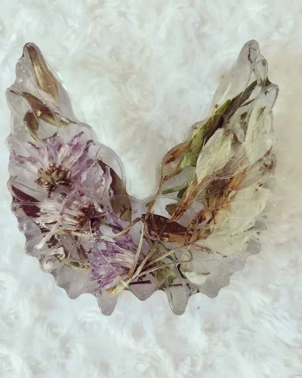 Transparent resin wings with embedded dried flowers on a soft white background.