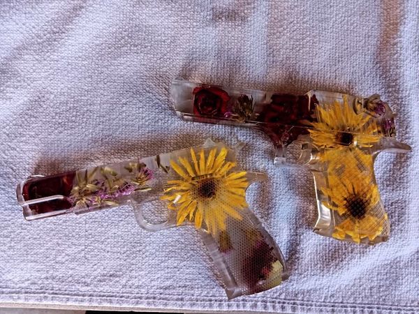 Two transparent resin guns with embedded yellow and red flowers.