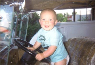 Smiling baby sitting on a truck seat holding the steering wheel.