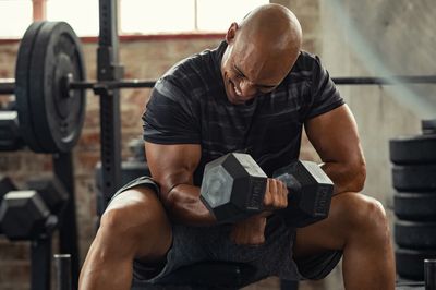 Man intensely lifting dumbbells in a gym, focusing on arm workout.