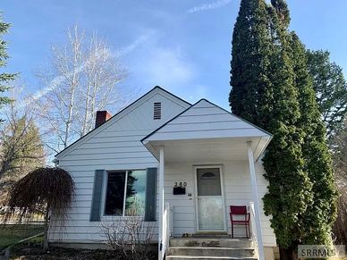Small white house with a front porch and tall tree beside it.
