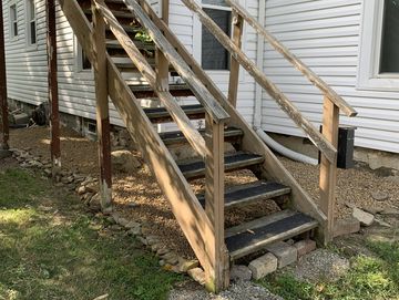 Worn wooden stairs with peeling paint on the side of a white house.