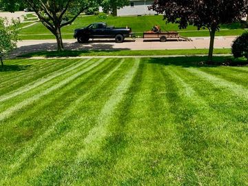Freshly mowed lawn with striped pattern and a black truck towing a trailer.