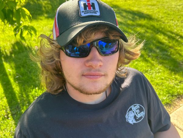Young man wearing sunglasses and a cap, relaxing outdoors on a sunny day.