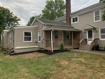 Suburban house with beige siding, a porch, and a small lawn under an overcast sky.