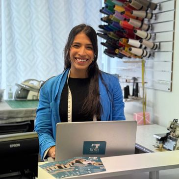 Smiling woman in blue jacket working at a sewing atelier with colorful threads.