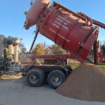 Large red industrial vacuum truck unloading sand outdoors.