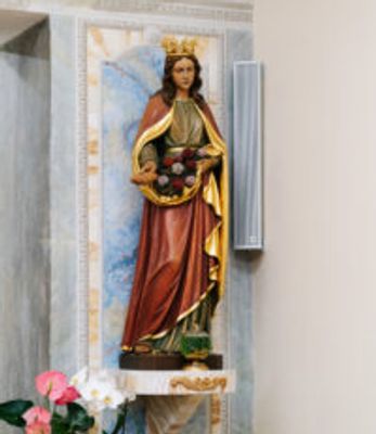 Statue of a crowned woman holding roses, placed on a pedestal in a church interior.