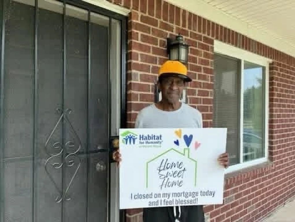 Man in yellow cap holding a sign about closing his mortgage with Habitat for Humanity.