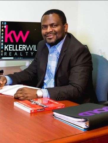 Man in business attire sitting at desk with Keller Williams Realty on screen.