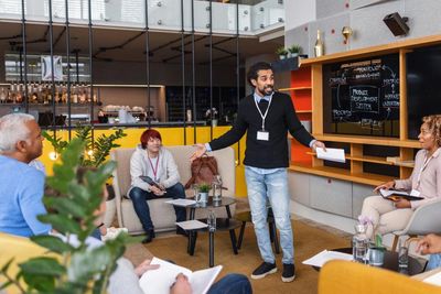 A man leads a team meeting in a modern office lounge area.
