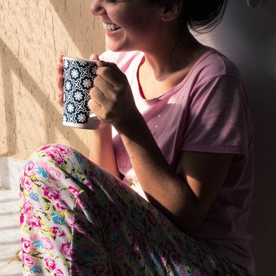 Woman enjoying a drink in floral pajamas and pink shirt.