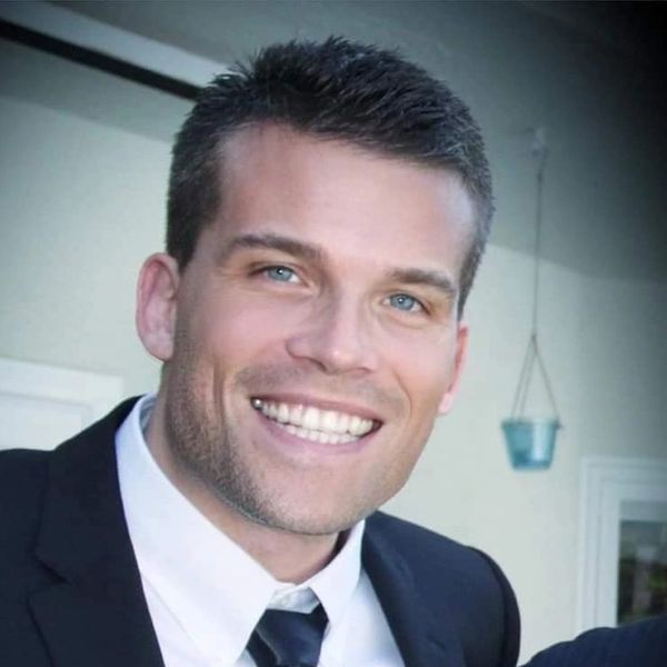 A smiling man in a suit with blue eyes and short hair.