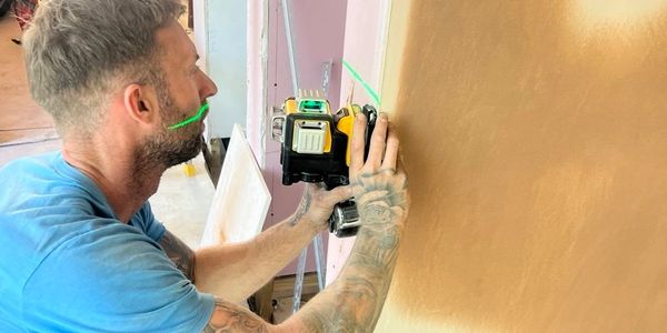 Man using a laser level tool to align a wall.