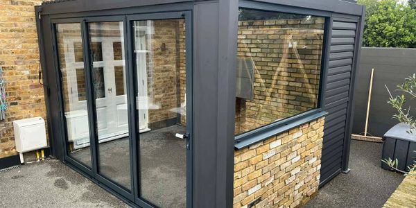 Modern outdoor glass conservatory with black frames and brick accents.