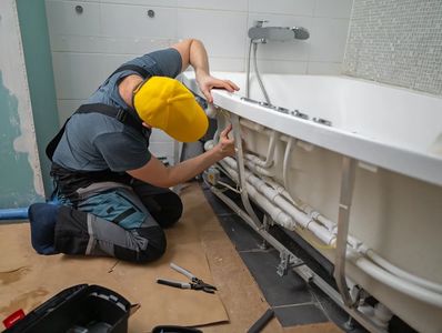 Plumber installing pipes behind a bathroom bathtub.