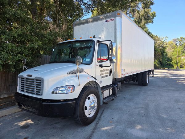 White delivery truck parked near trees on a sunny day.