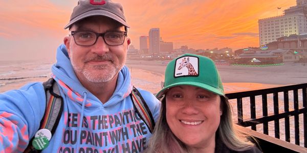 Two people smiling at sunset on a beach pier.